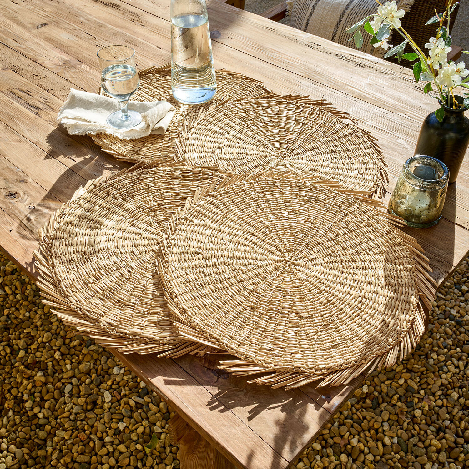 Platzset 4er Set Nuviras Runde Tischsets aus natürlichem Geflecht auf einem Holztisch im Außenbereich