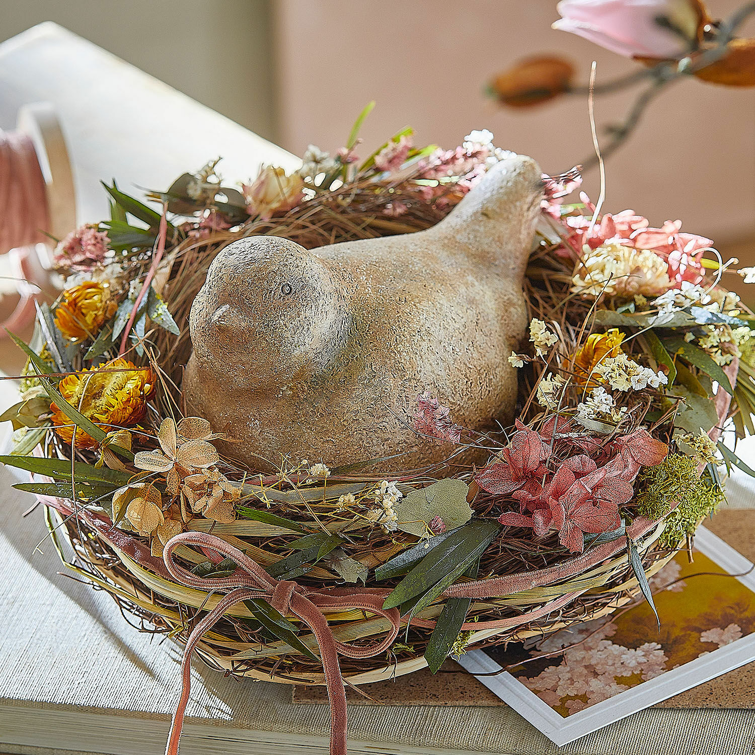 Deko Figur Nafisah Dekorativer Steinvogel im Weidenkorb mit getrockneten Blumen auf einem Tisch