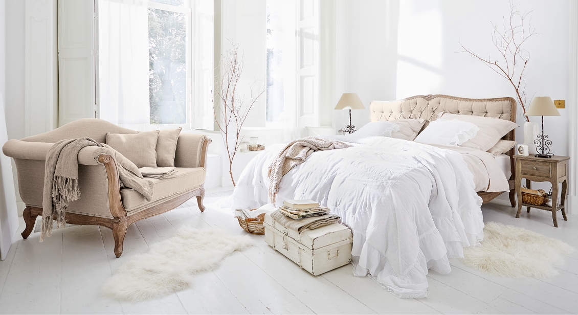Gemütliches Schlafzimmer mit beigem Polsterbett und Vintage-Sofa auf hellem Holzboden