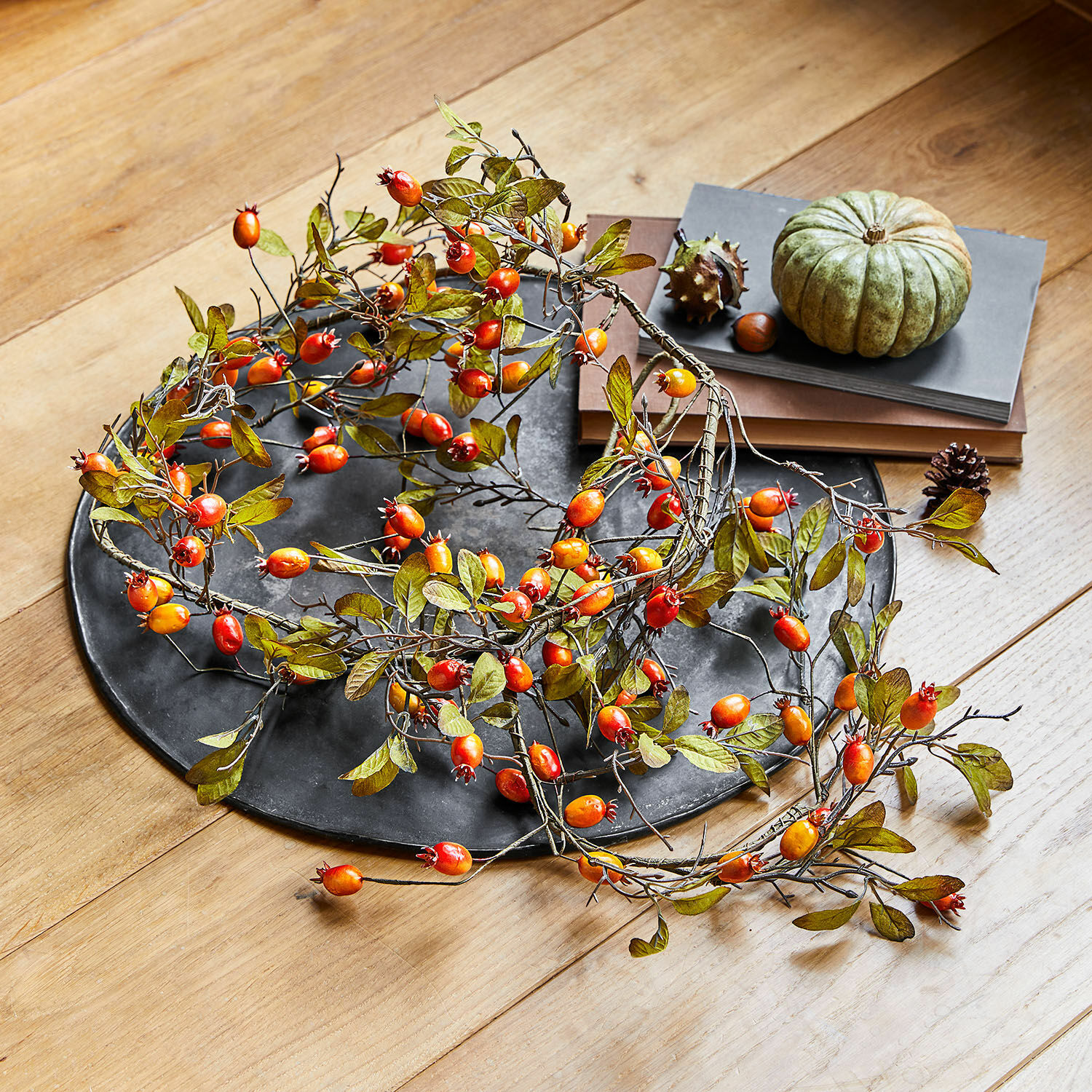 Dekorativer Kranz mit roten und orangen Beeren auf schwarzem Tablett auf Holztisch