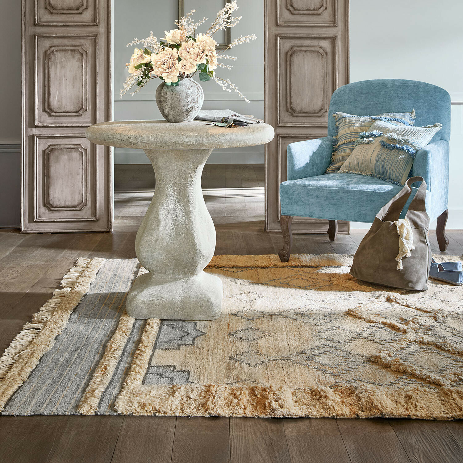 Runder grauer Betontisch mit Blumenvase neben blauem Sessel und gemustertem Teppich