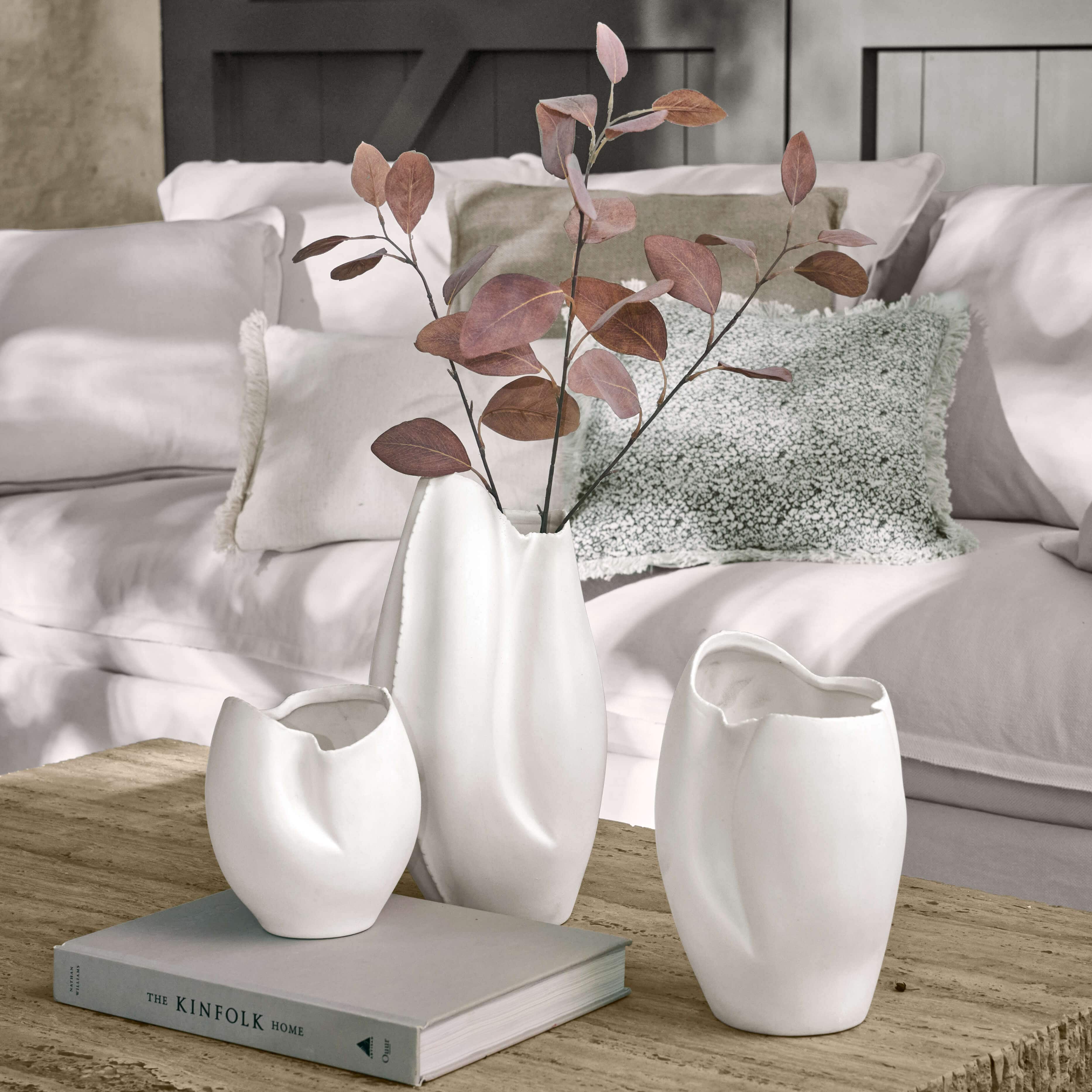 Set aus drei weißen Keramikvasen mit unregelmäßiger Form auf Holztisch im Wohnzimmer