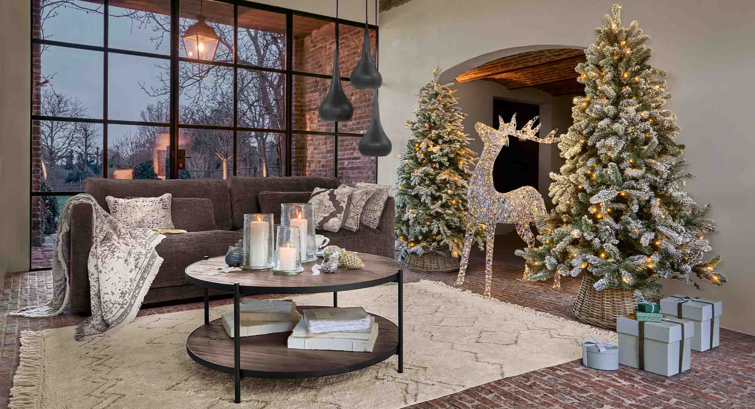 Gemütliches Wohnzimmer mit braunem Sofa, beleuchteten Weihnachtsbäumen und LED-Dekorhirsch