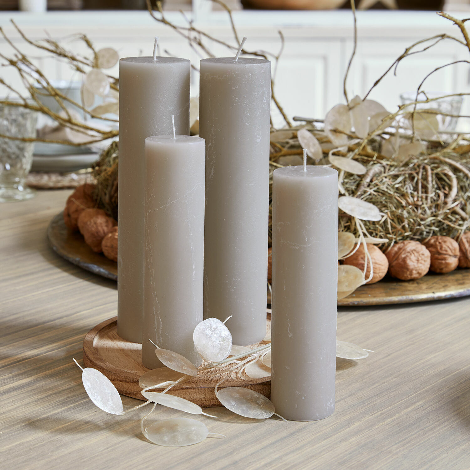 Set aus vier grauen Wachskerzen auf Holzplatte, natürliche Tischdekoration mit Zweigen