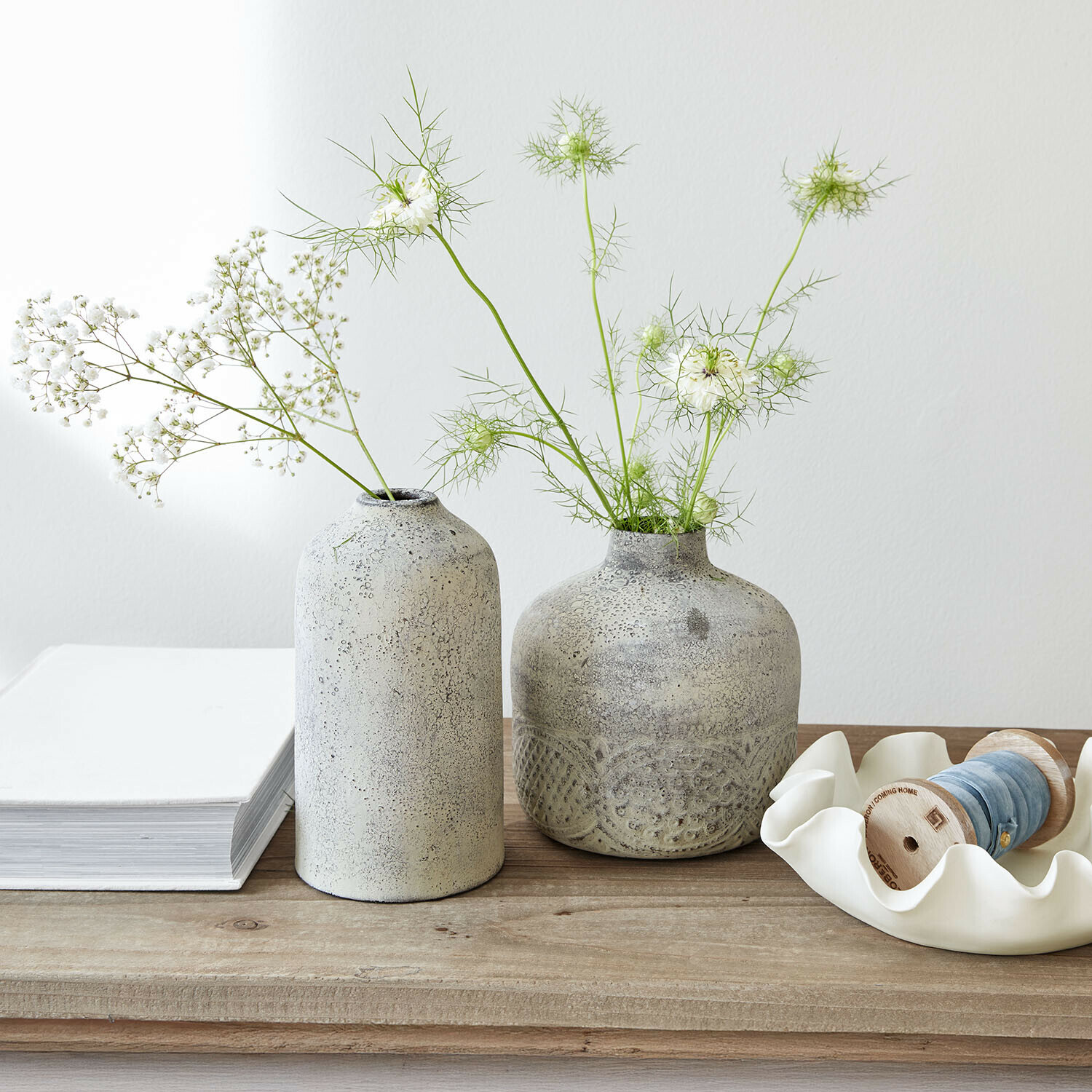 Zwei graue Keramikvasen mit zarten weißen Blumen auf hellem Holztisch dekorativ arrangiert