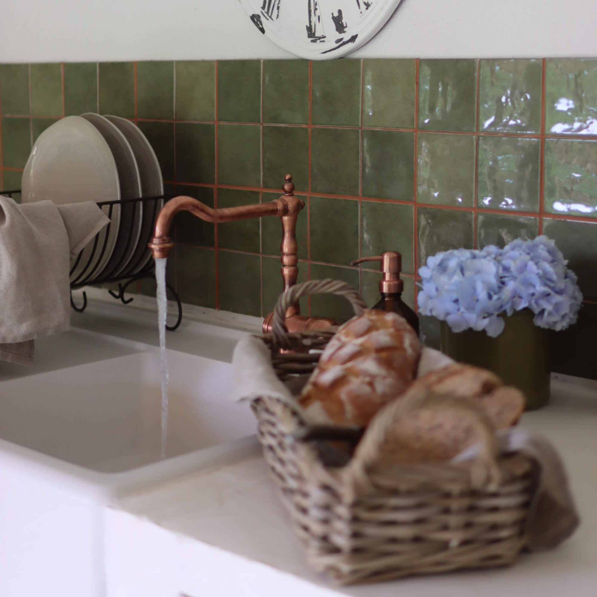 Küche mit kupfernem Wasserhahn, grünen Fliesen, Brotkorb und blauen Blumen als Dekor