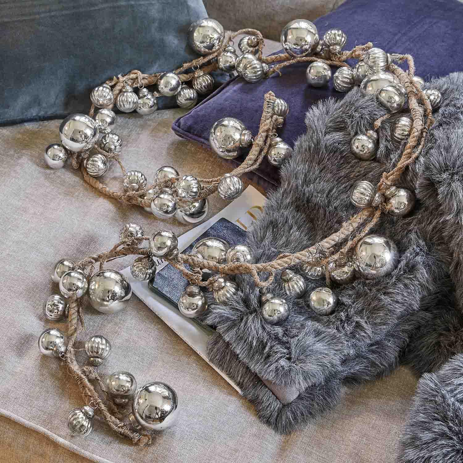 Dekorative Kette mit silbernen Metallkugeln an Juteseil auf weichen Kissen und Fell