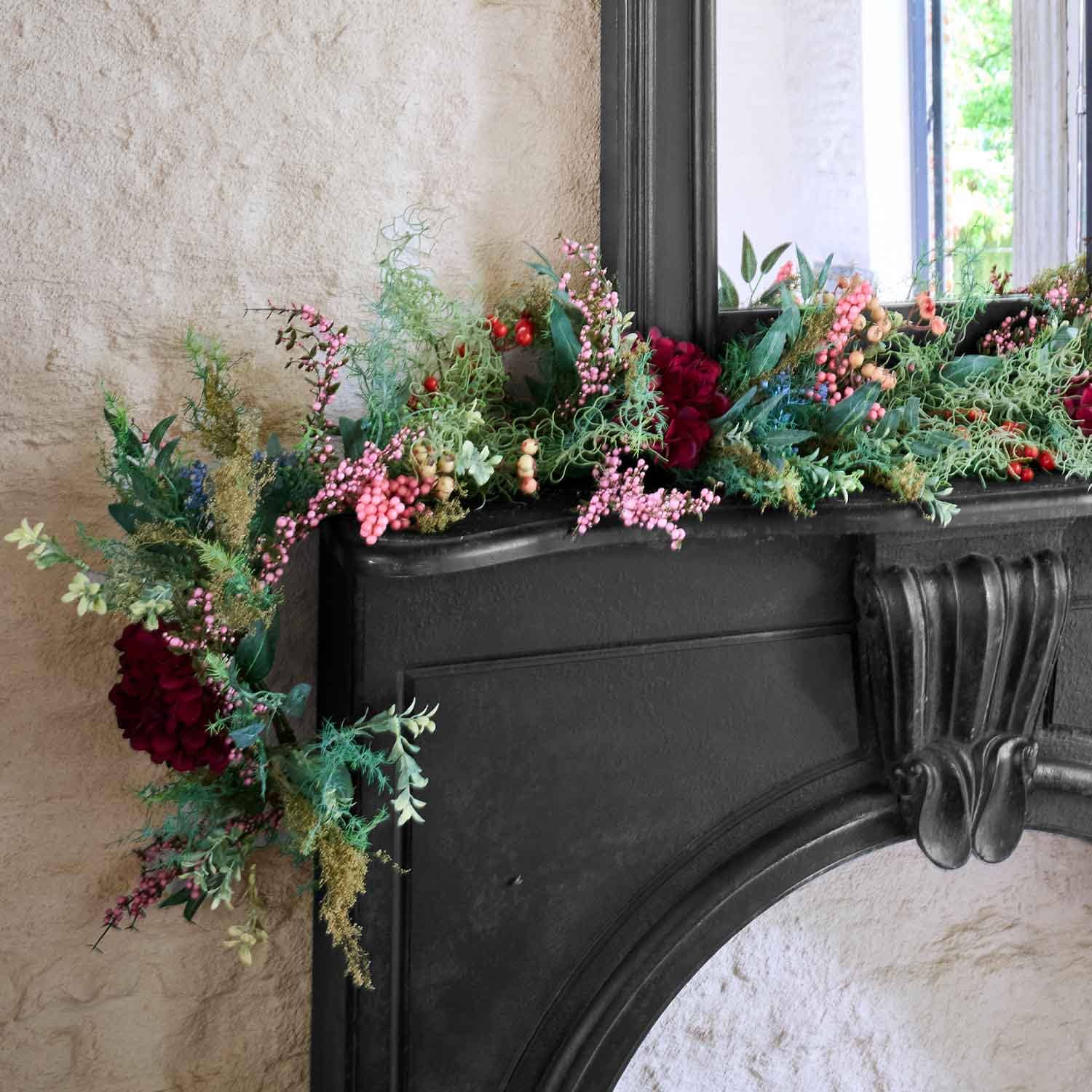 Dekorativer Kranz mit roten und rosa Beeren sowie grünem Laub auf schwarzem Kamin