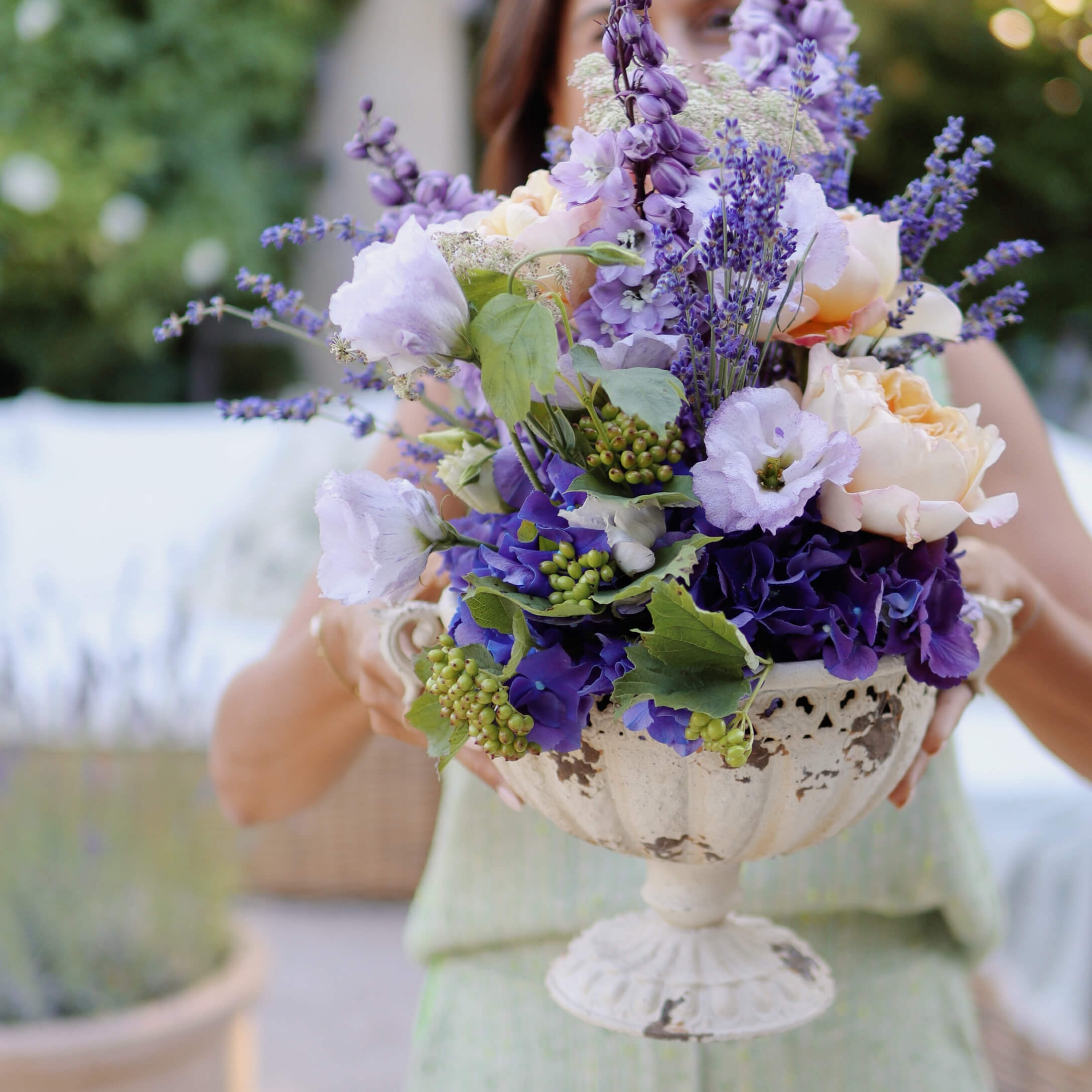 Strauß aus violetten und cremefarbenen Blumen in weißer, dekorativer Keramikvase auf Fuß
