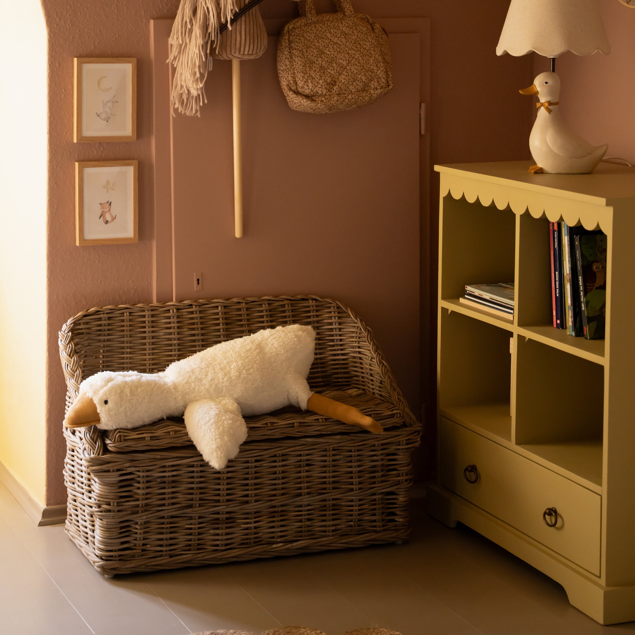 Wickerbank mit langem weißem Plüsch-Entenkissen in gemütlichem Kinderzimmer mit gelbem Regal