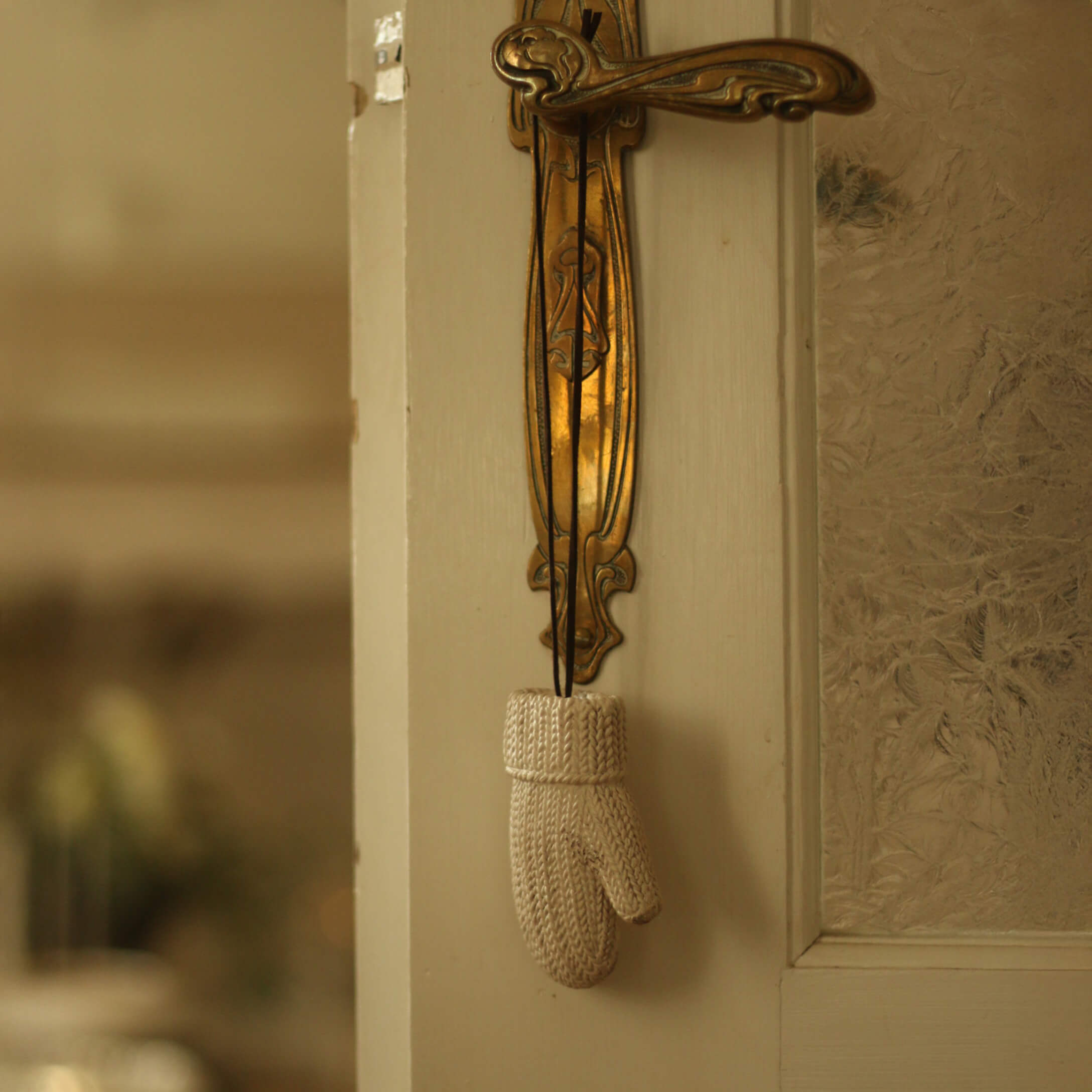 Weiße gestrickte Dekohandschuh an verziertem goldfarbenem Messing-Türgriff hängend