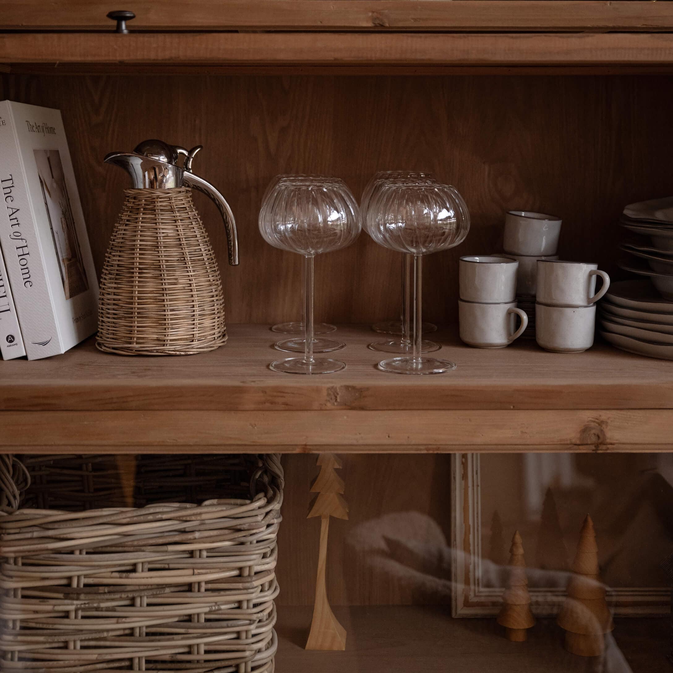 Gläser mit geriffeltem Muster auf Holzregal mit Korbkanne und weißen gestapelten Tassen