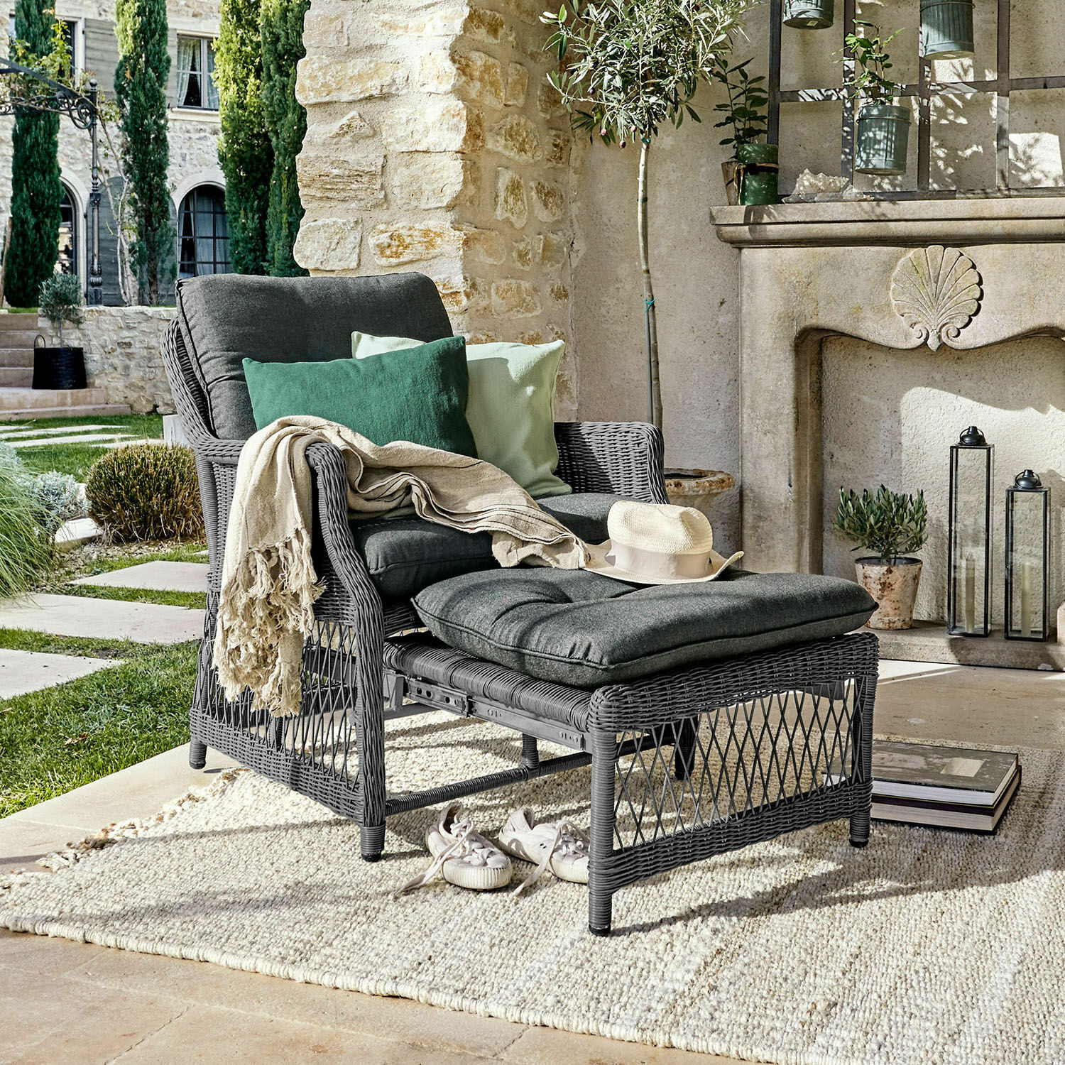 Sessel Howe Grauer Rattansessel mit Fußhocker und dunkelgrauen Kissen, dekoriert mit grünen Kissen auf der Terrasse
