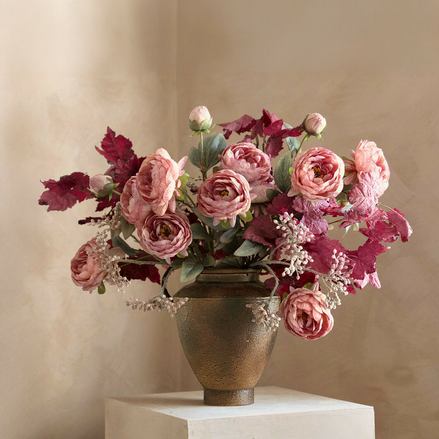 Strauß aus rosa Rosen und roten Blättern in braunem Keramikvase vor hellem Hintergrund