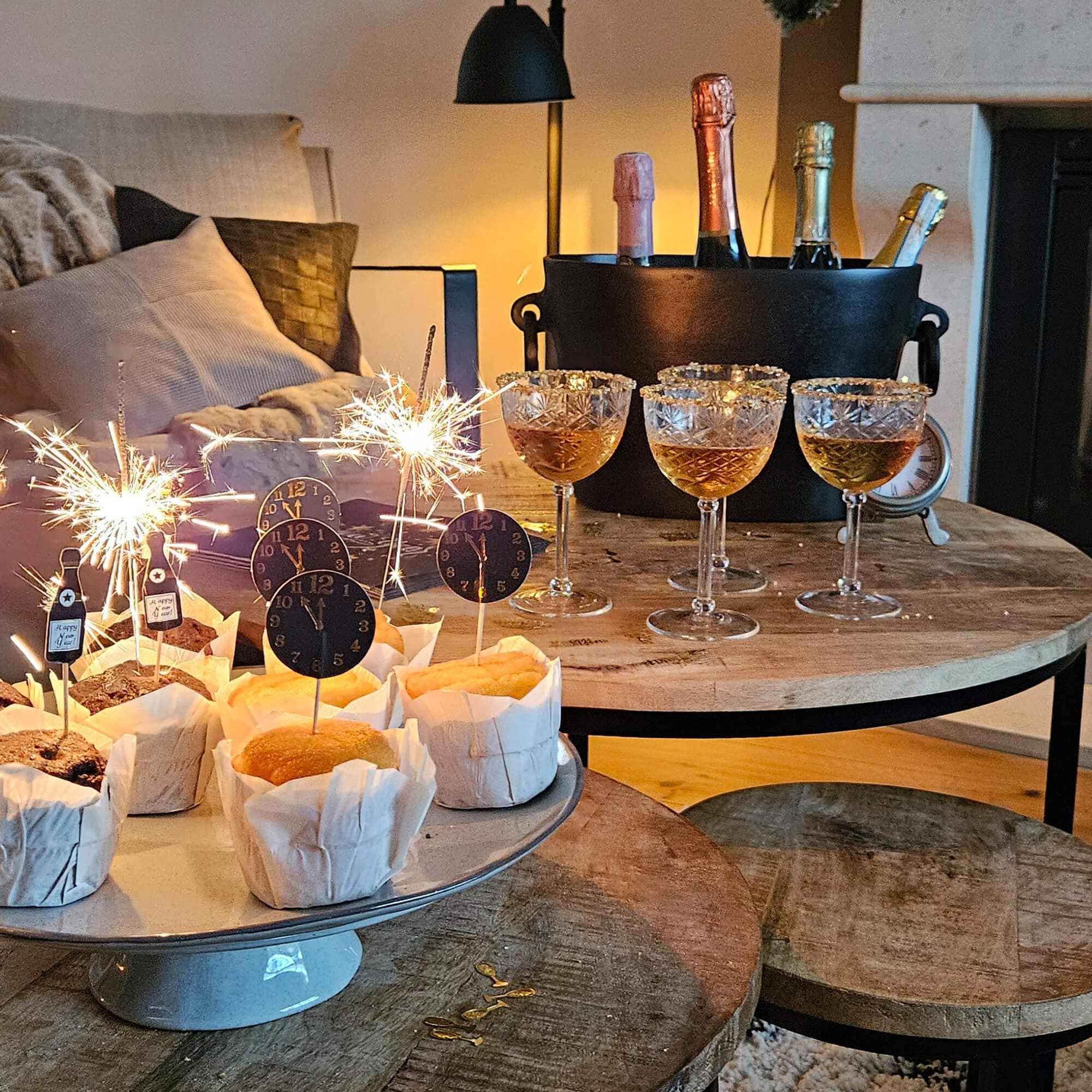 Feier mit Muffins, Gläsern und Flaschen im Eimer auf Holztisch in gemütlichem Raum