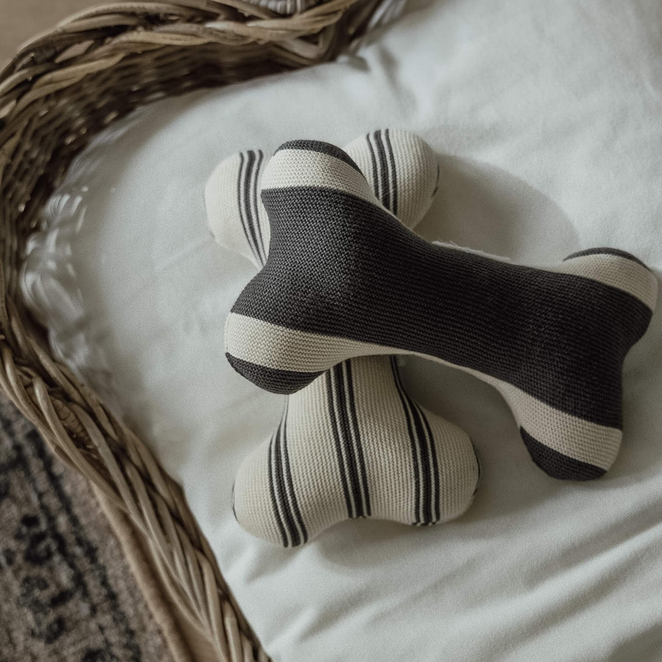 Zwei gestrickte Knochen-Spielzeuge in schwarz-weißen Streifen auf weißem Untergrund im Korb