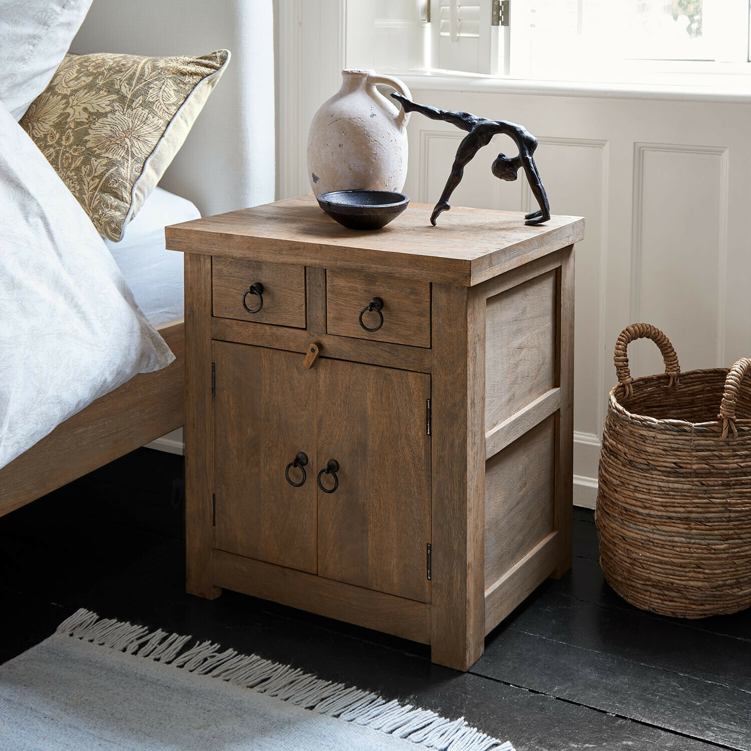 Nachttisch aus Holz in Naturfarbe mit Metallgriffen und dekorativen Objekten auf der Oberfläche im Schlafzimmer