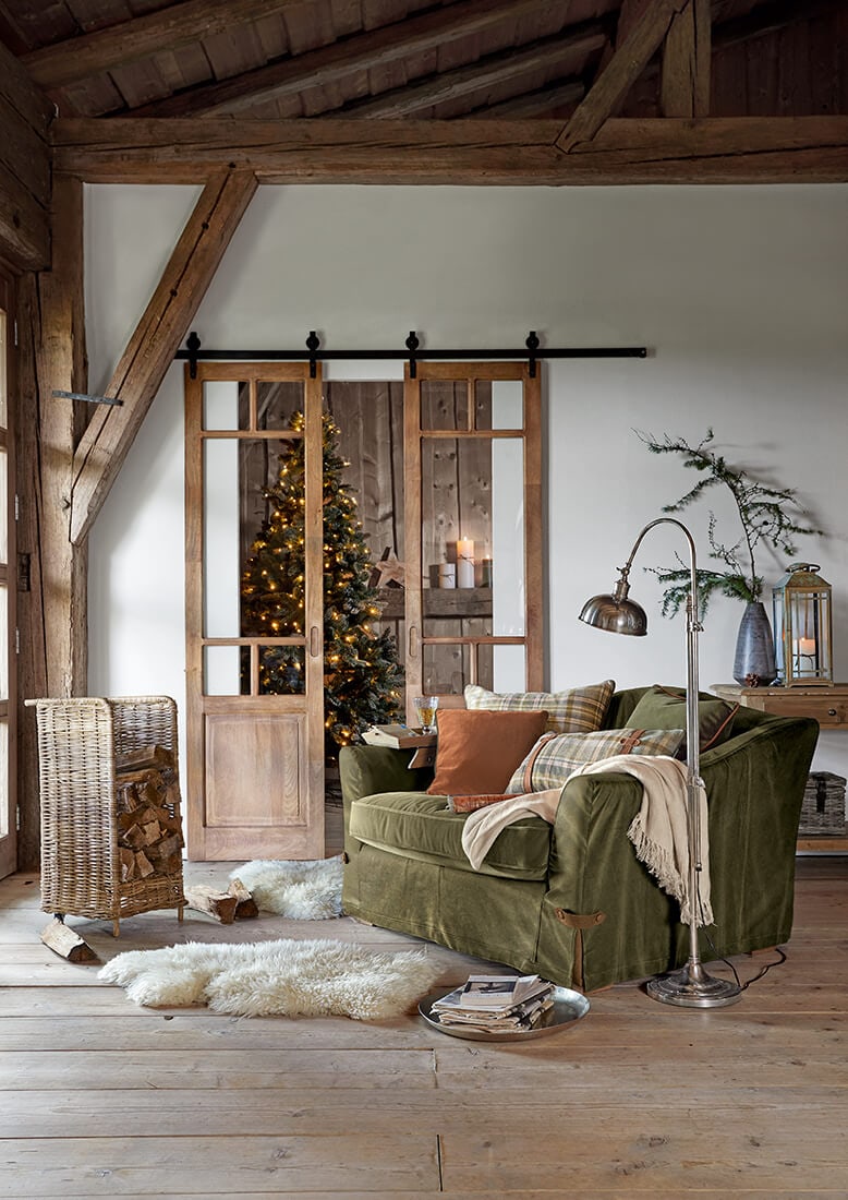 Gemütliches Wohnzimmer mit grünem Sofa, Holz-Schiebetüren und geschmücktem Weihnachtsbaum im Hintergrund