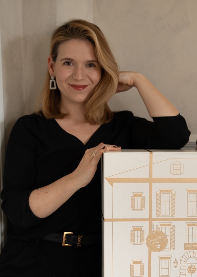 Frau in schwarzer Bluse mit Geschenkbox, bedruckt mit Hausmotiv, weihnachtliches Design