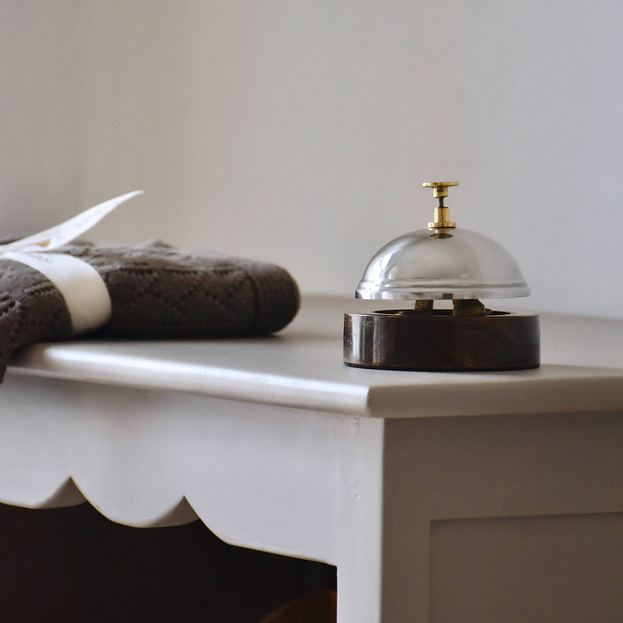 Metallklingel auf Holzsockel auf weißem Tisch neben brauner Strickdecke