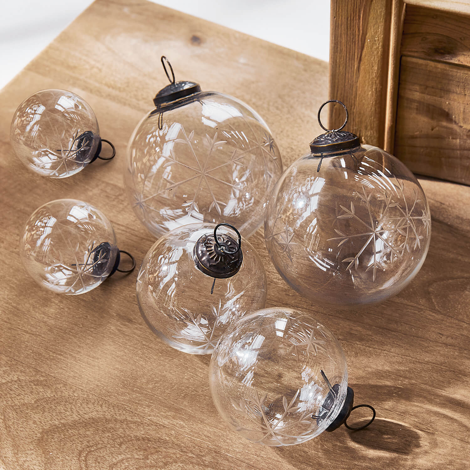 Transparente Glas-Weihnachtskugeln mit graviertem Schneeflockenmuster auf Holztisch, festliche Deko