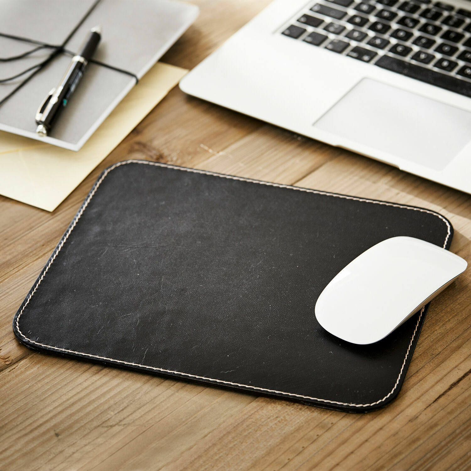 Mauspad Dehaan Schwarze Leder-Mausunterlage mit weißer Naht auf Holztisch neben Laptop