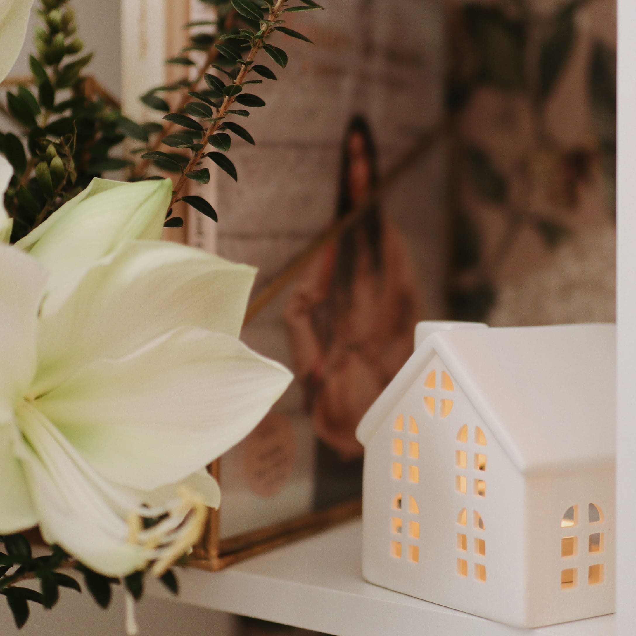 Weiße Keramikhaus-Dekoration mit Beleuchtung und weißen Blumen auf Regal, festliche Stimmung