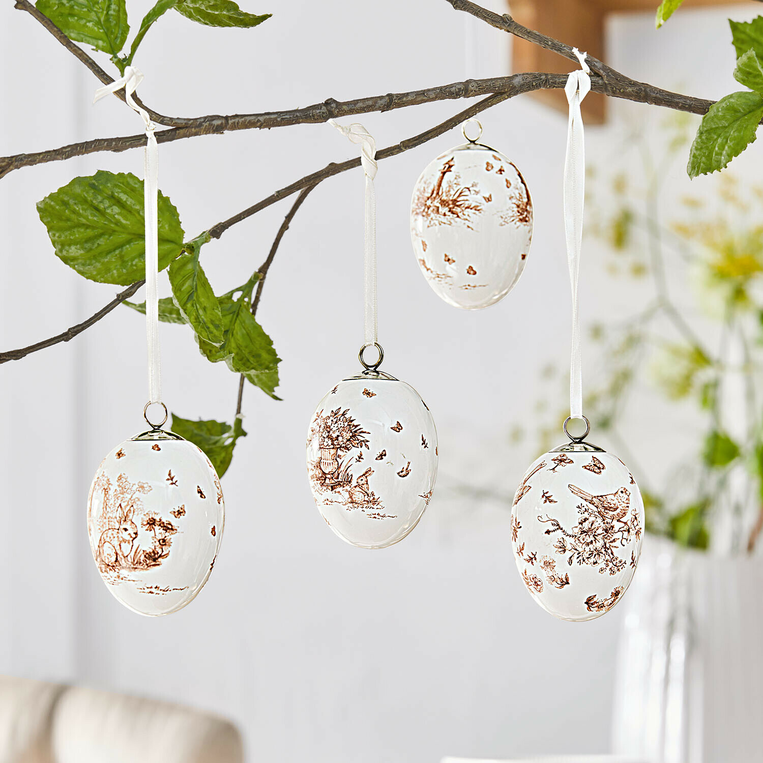 Weiße Keramikeier mit braunen Tier- und Pflanzenmotiven, an einem Ast hängend, Osterdekoration