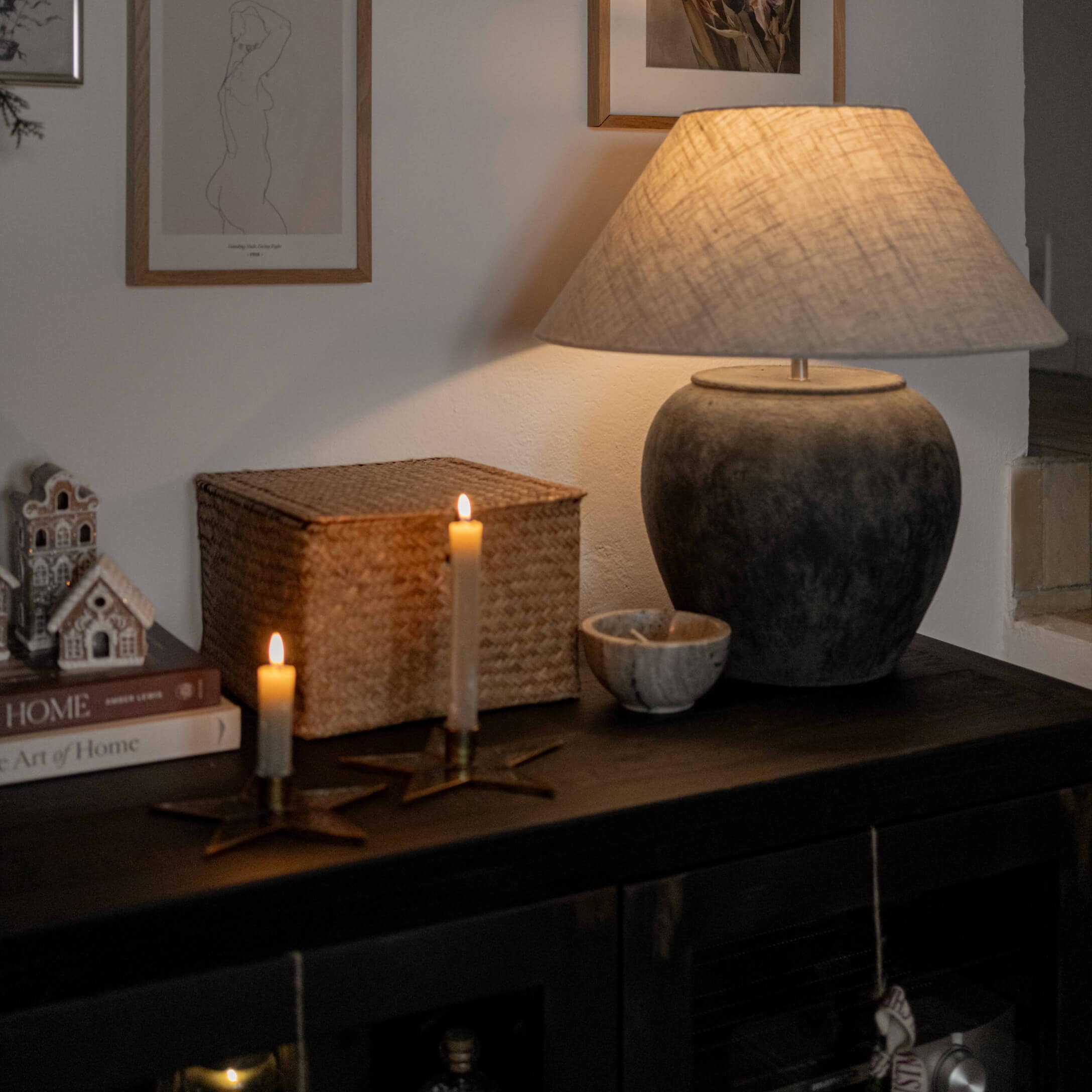 Tischlampe aus dunkelgrauer Keramik mit beigem Lampenschirm auf dunklem Möbel mit Kerzen und Dekorationen