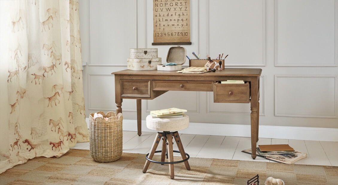 Holzschreibtisch mit drei Schubladen und hell gepolstertem Hocker in gemütlichem Lernzimmer