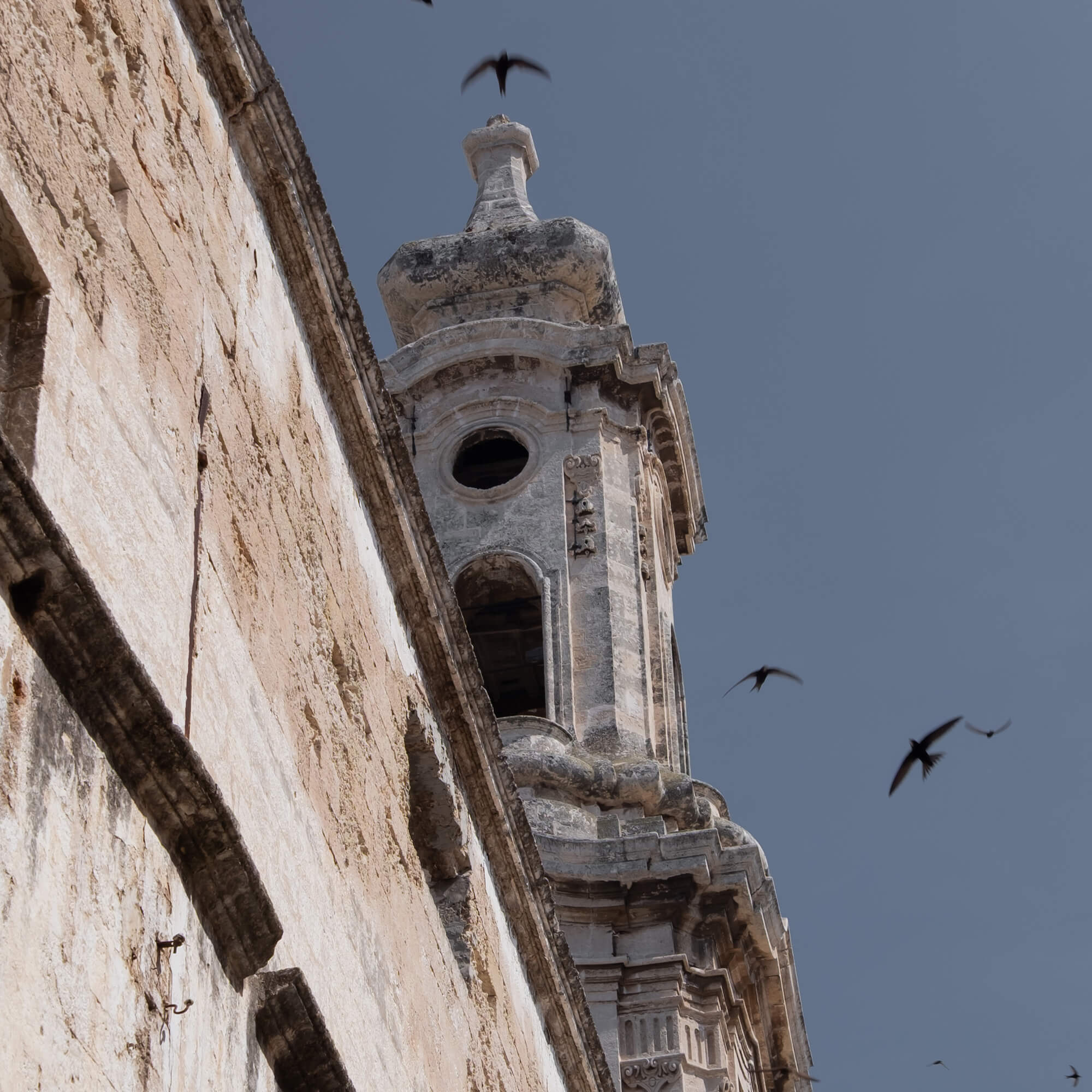 Blick auf einen alten steinernen Turm mit Vögeln vor blauem Himmel