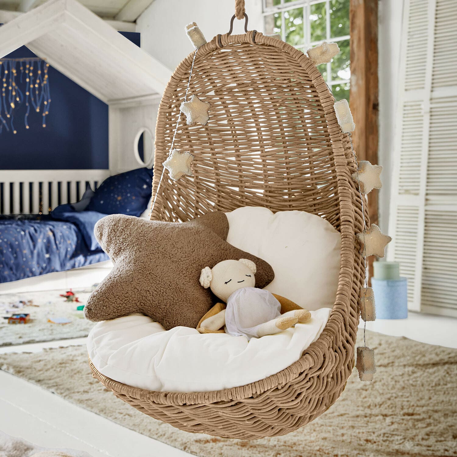 Hängesessel aus Rattan mit weißem Kissen und Stern-Lichterkette im Kinderzimmer
