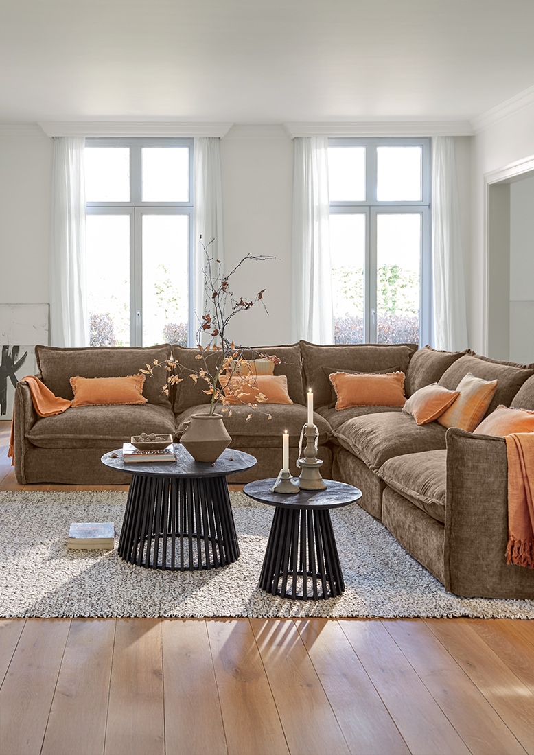 Gemütliches Wohnzimmer mit brauem Ecksofa und schwarzen Beistelltischen auf hellem Teppich