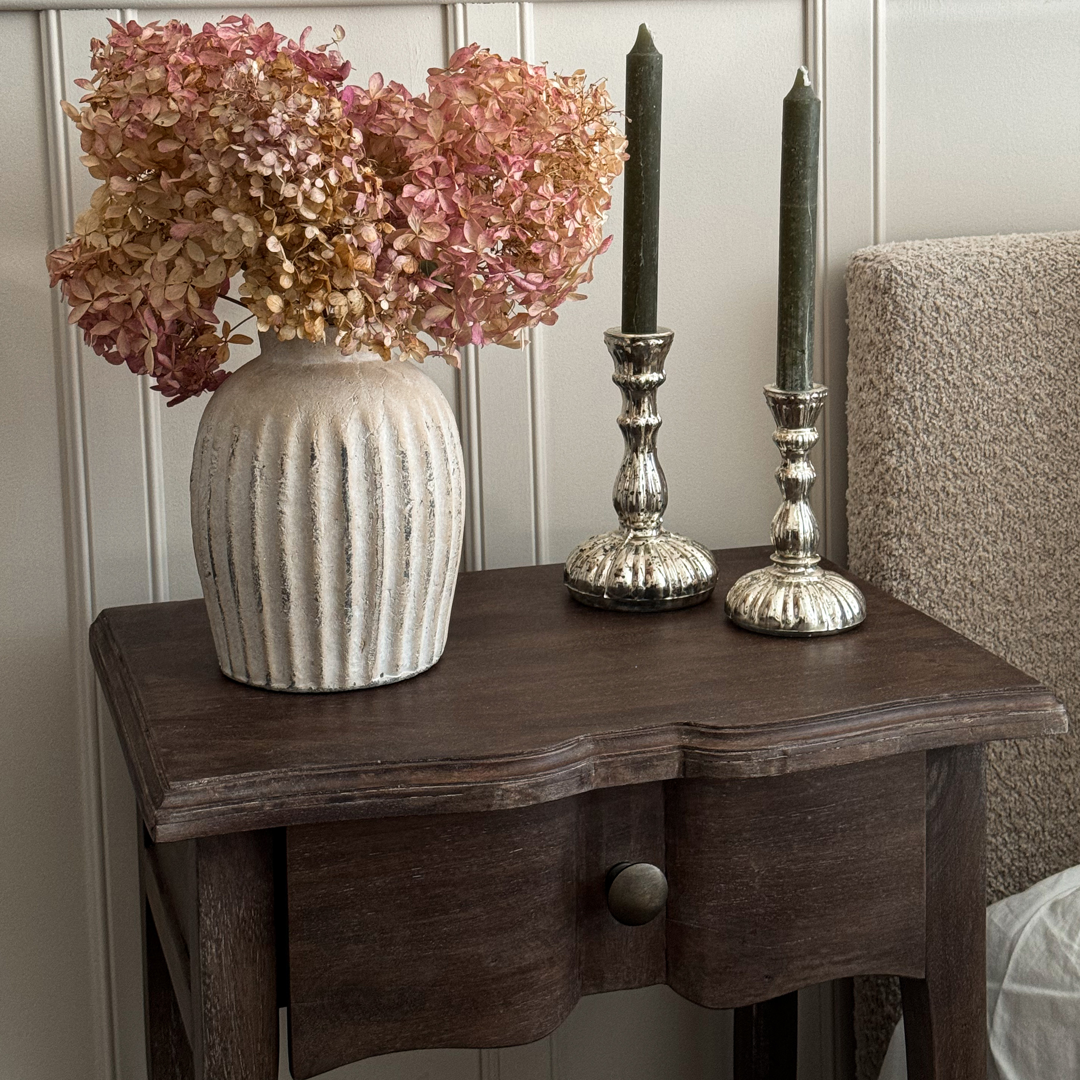 Beiger Keramikvase mit getrockneten rosa Blüten auf dunklem Holztisch als Dekoration