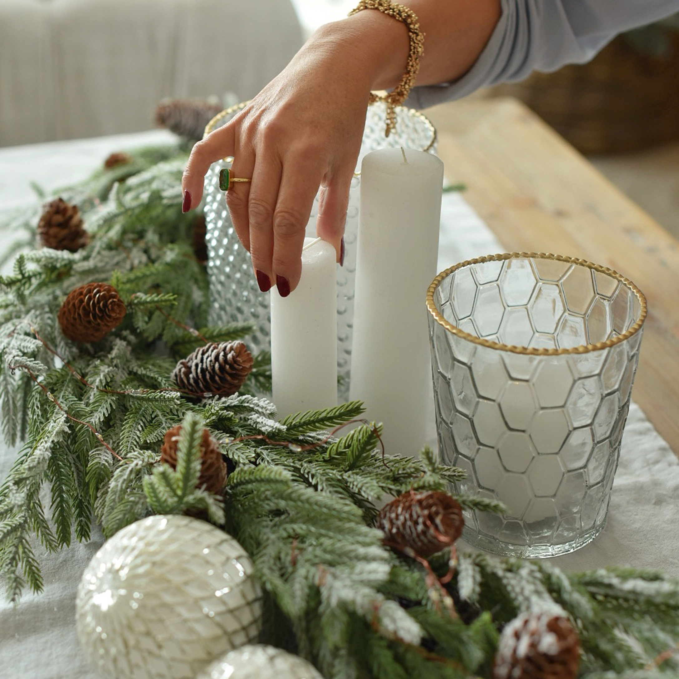Weihnachtsdekoration mit weißen Kerzen, Glaswindlicht mit goldenem Rand und grünen Zweigen mit Zapfen