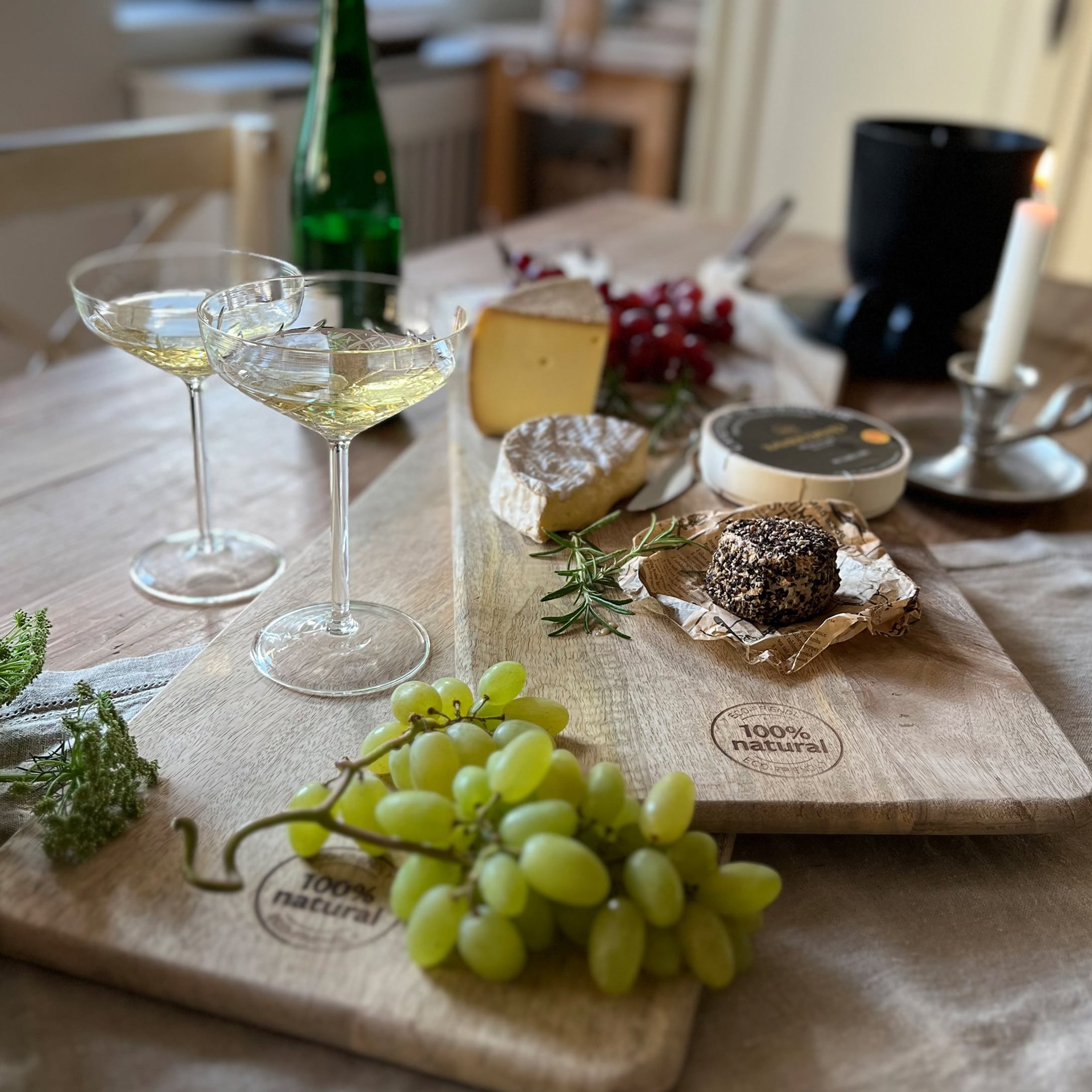 Schneidebrett aus Naturholz mit Trauben, verschiedenen Käsesorten und Weingläsern auf Holztisch