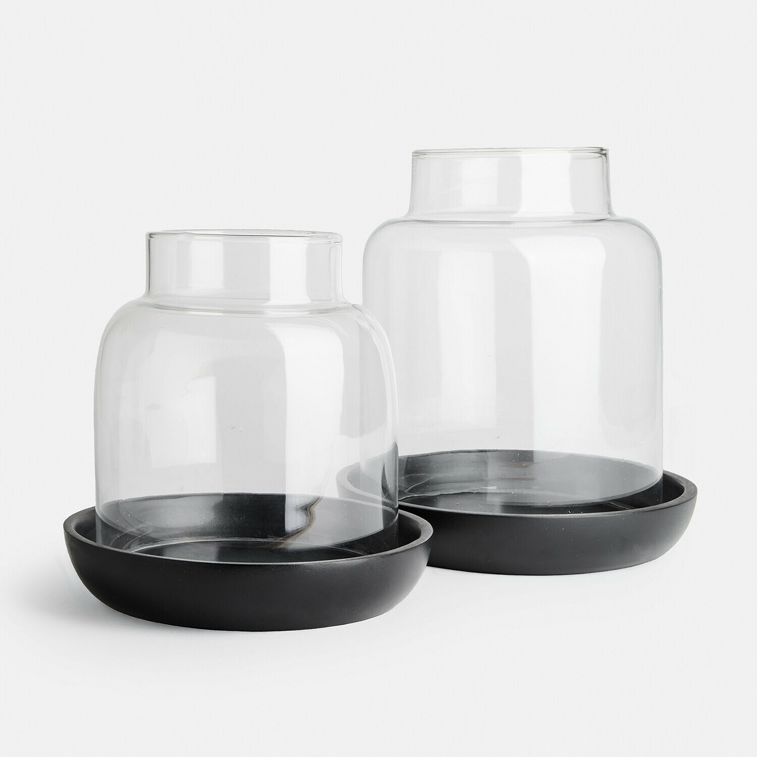 Zwei transparente Glaslaternen auf schwarzen Metallständern als moderne Wohnraumdekoration