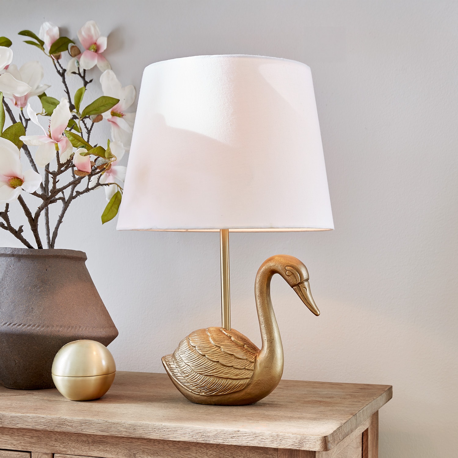 Goldene Tischlampe in Schwanform mit weißem Lampenschirm auf Holztisch mit Blumenarrangement