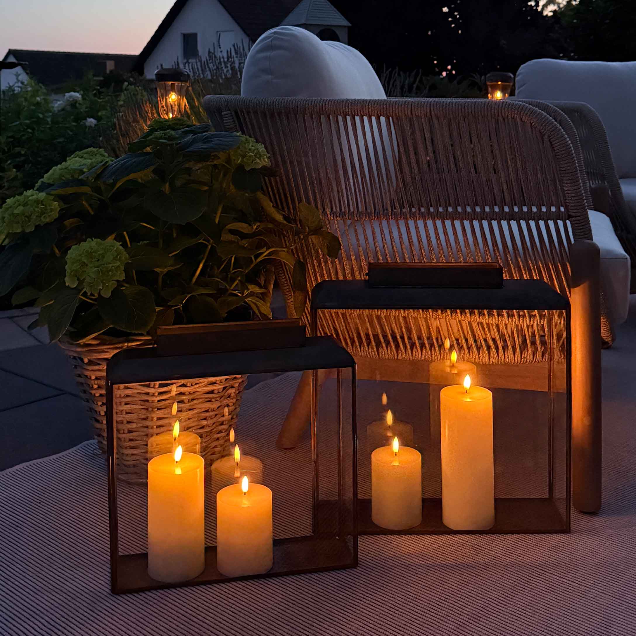 Stimmungsvolle Beleuchtung mit Laternen und Kerzen auf Terrasse mit Korbsessel und weißem Kissen