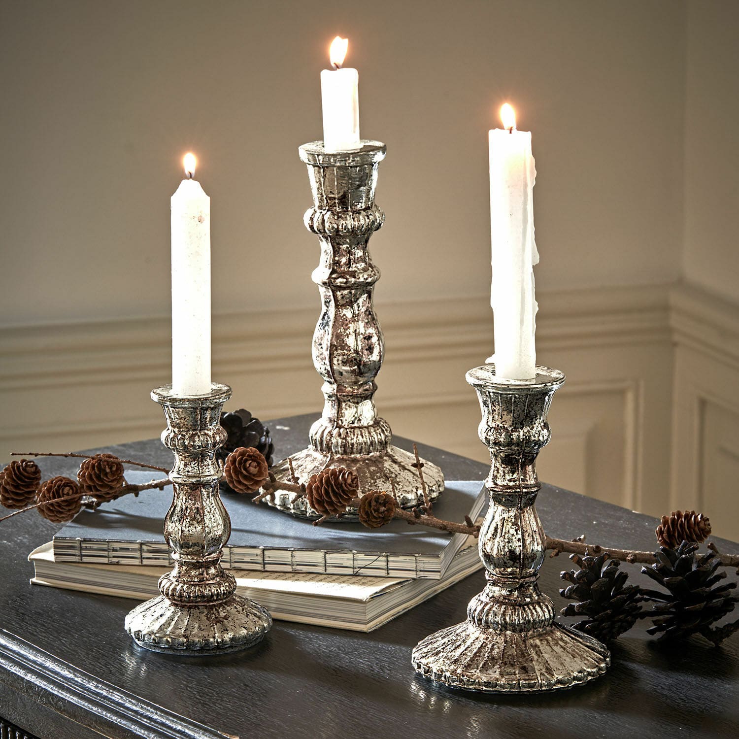 Kerzenständer 3er Set Favalina Drei vintage Metall-Kerzenhalter in Silber mit weißen Kerzen auf dunklem Tisch mit Kiefernzapfen dekoriert