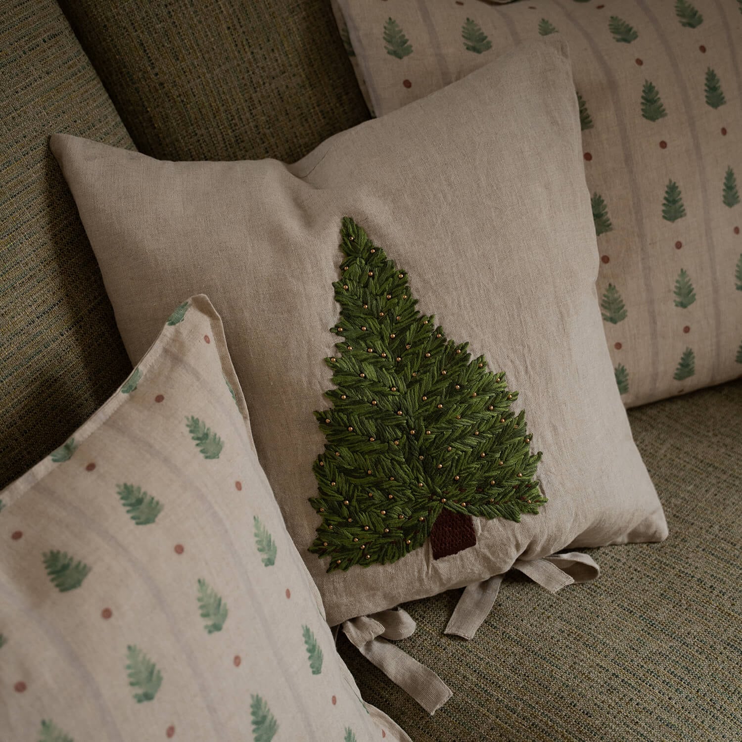 Beige Leinenkissen mit grünem besticktem Tannenbaum und goldenen Perlen auf Sofa