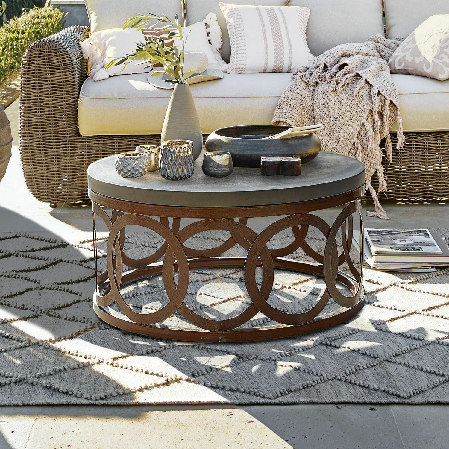 Couchtisch Boécourt Runder Couchtisch mit rostfarbener Metallbasis und grauer Tischplatte auf Terrasse mit Korbsofa