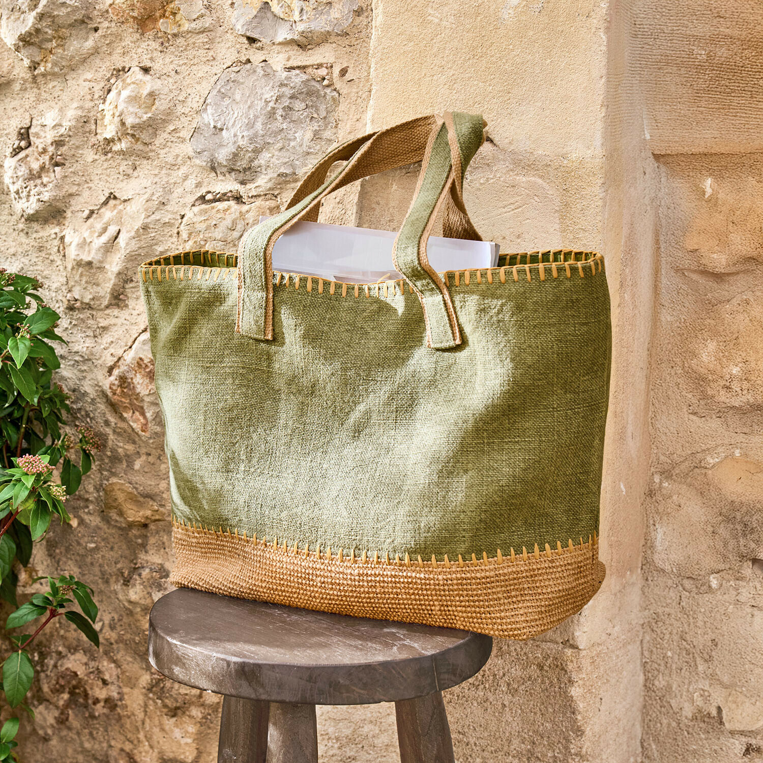 Tasche Yarrowton Grüne Jutetasche mit braunen Details auf einem Holzschemel vor einer Steinwand