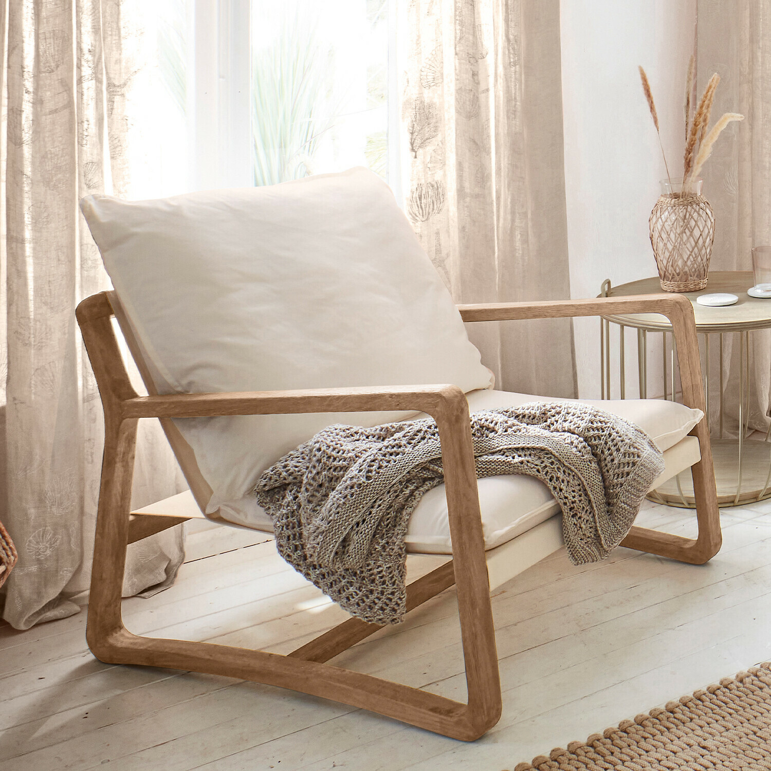 Sessel Jowna Sessel aus hellem Holz mit cremefarbenem Kissen und grauer Strickdecke in hellem Wohnzimmer