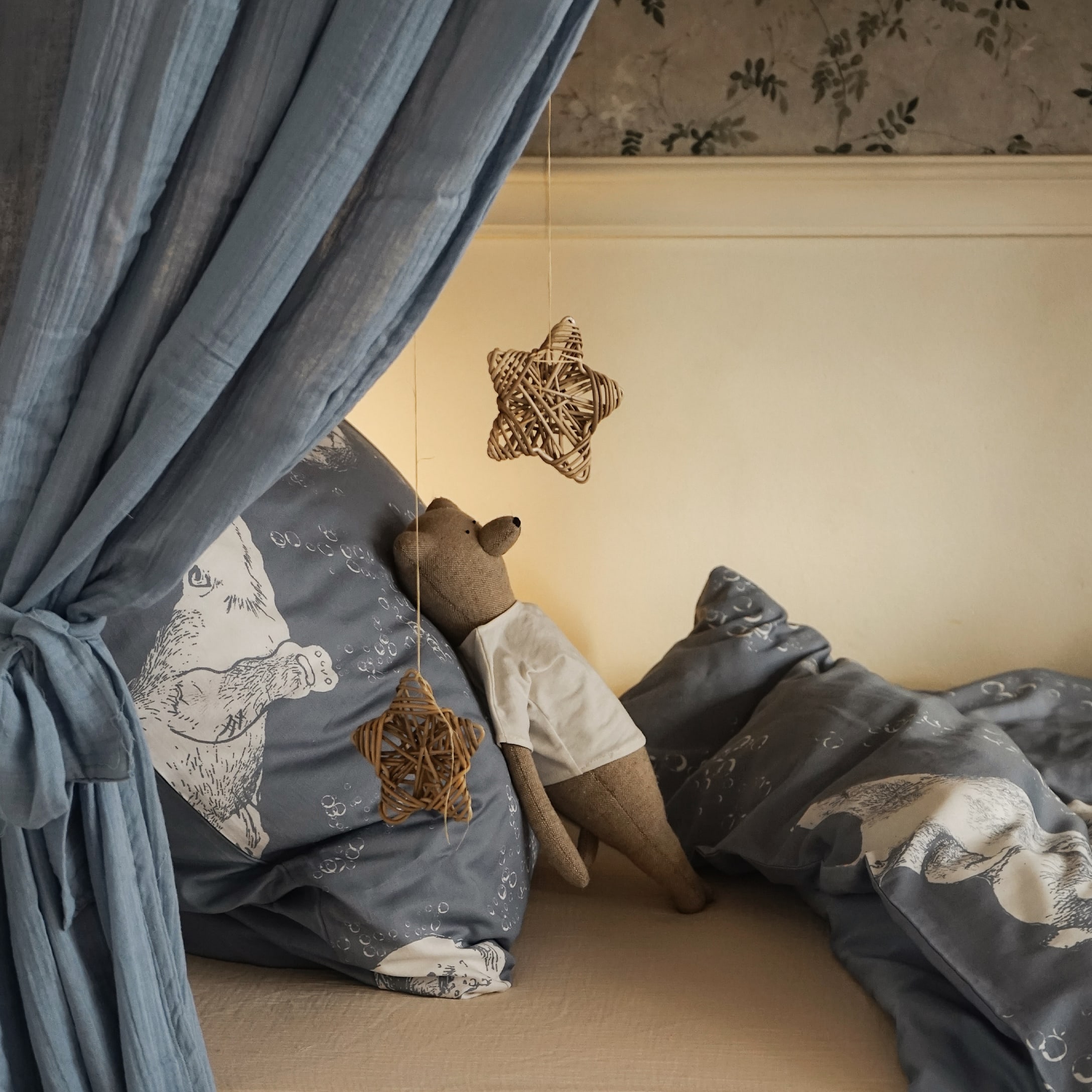 Gemütliches Bett mit blauem Bären-Motiv-Bettwäsche und braunem Stoffbären mit weißem T-Shirt