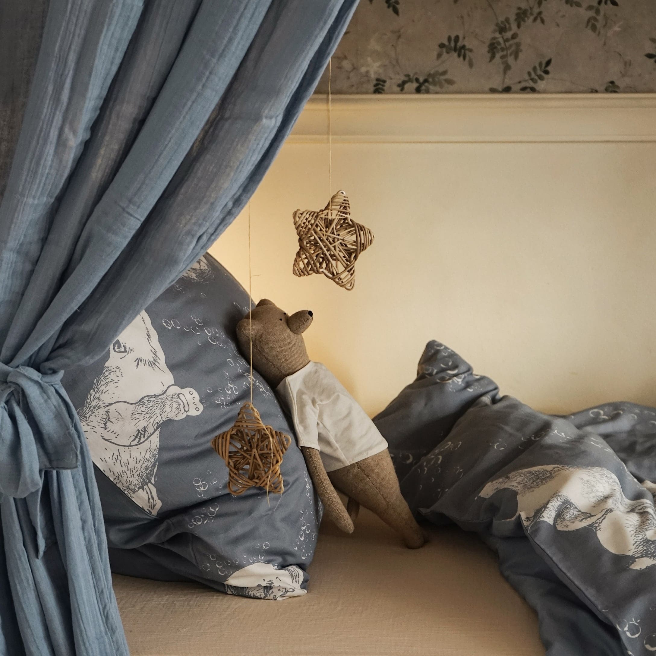 Gemütliches Bett mit blauem Bären-Motiv-Bettwäsche und braunem Stoffbären mit weißem T-Shirt
