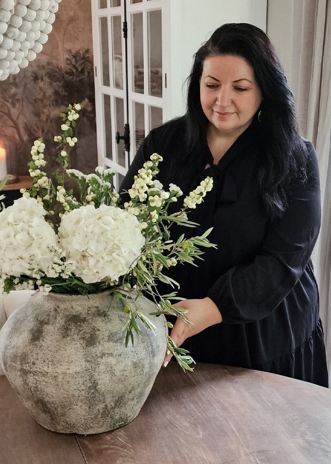 Frau arrangiert weißen Blumenstrauß in großem grauem Keramikvase auf Holztisch