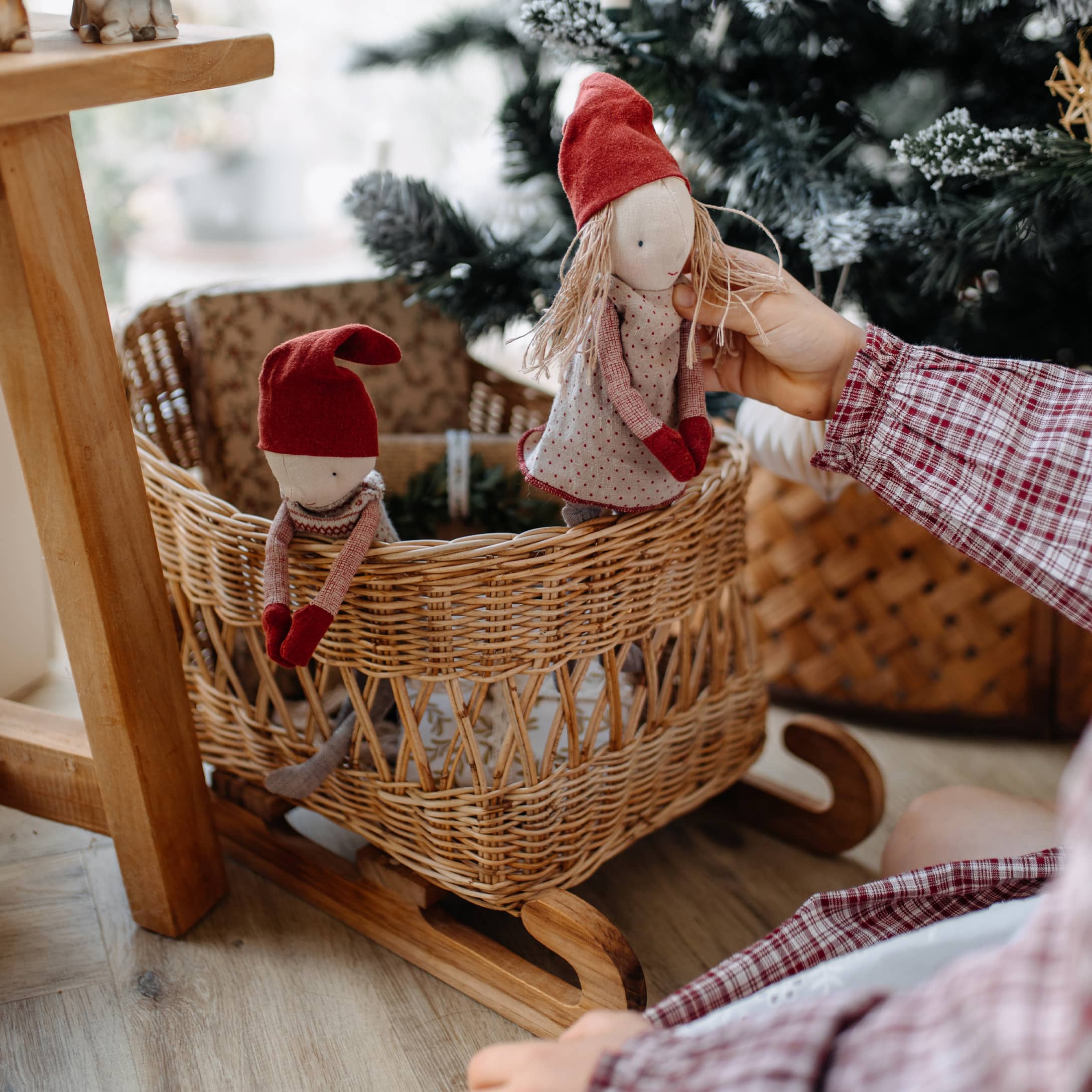 Holzschaukel mit Korb aus Weide und zwei Puppen mit roten Mützen, weihnachtliche Dekoration