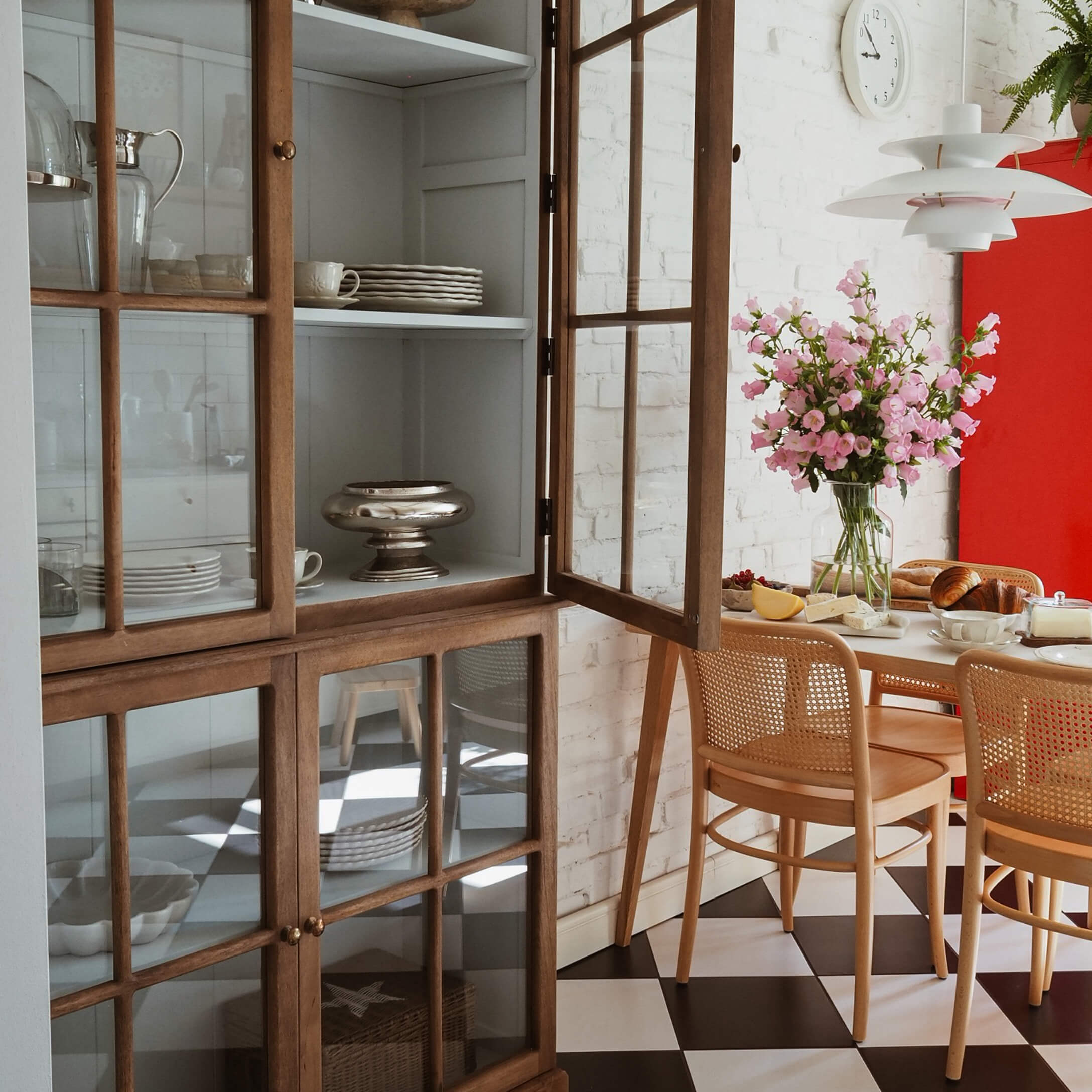 Helle Esszimmer mit Holzvitrine, rosa Blumen und schwarz-weiß kariertem Bodenbelag