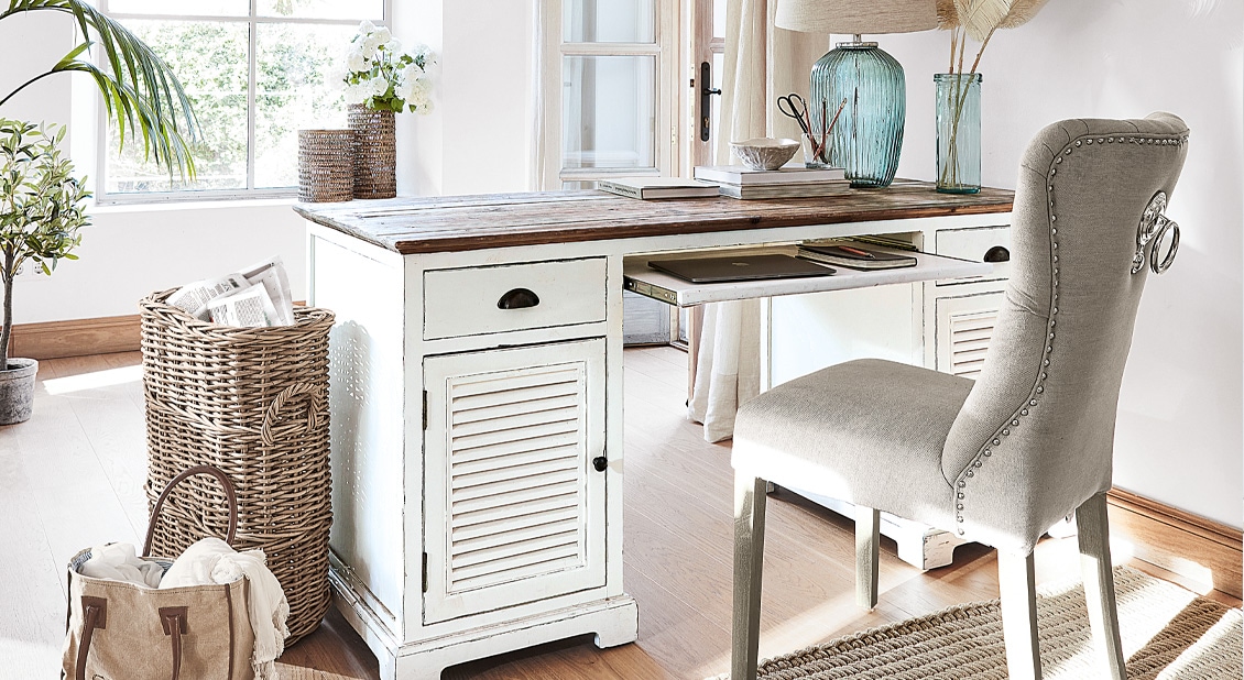 Weißes Holzschreibtisch im Shabby-Chic-Stil mit Schubladen und grauem Polsterstuhl in hellem Raum